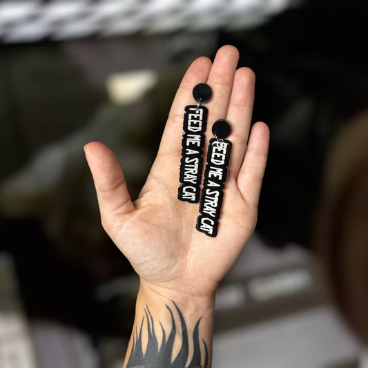 American Psycho Feed Me a Stray Cat ATM resin statement earrings being held