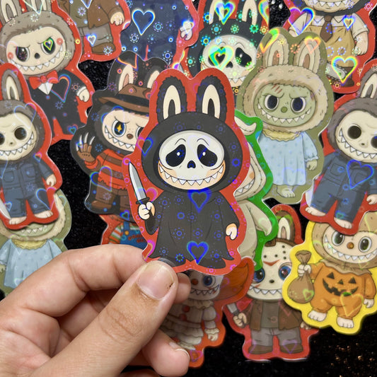 Hand holding a sticker of a Scream Ghostface Labubu sticker, surrounded by other colorful stickers on a black background