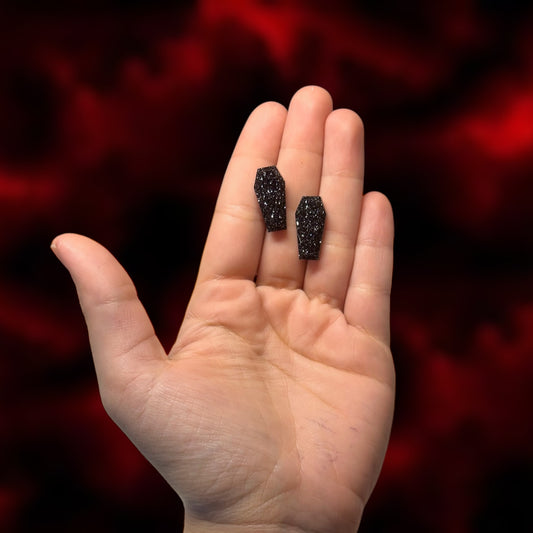 Glittery black coffin resin stud earrings being held