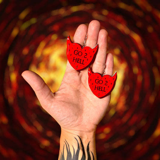 Go 2 Hell demon horns heart-shaped resin statement earrings being held