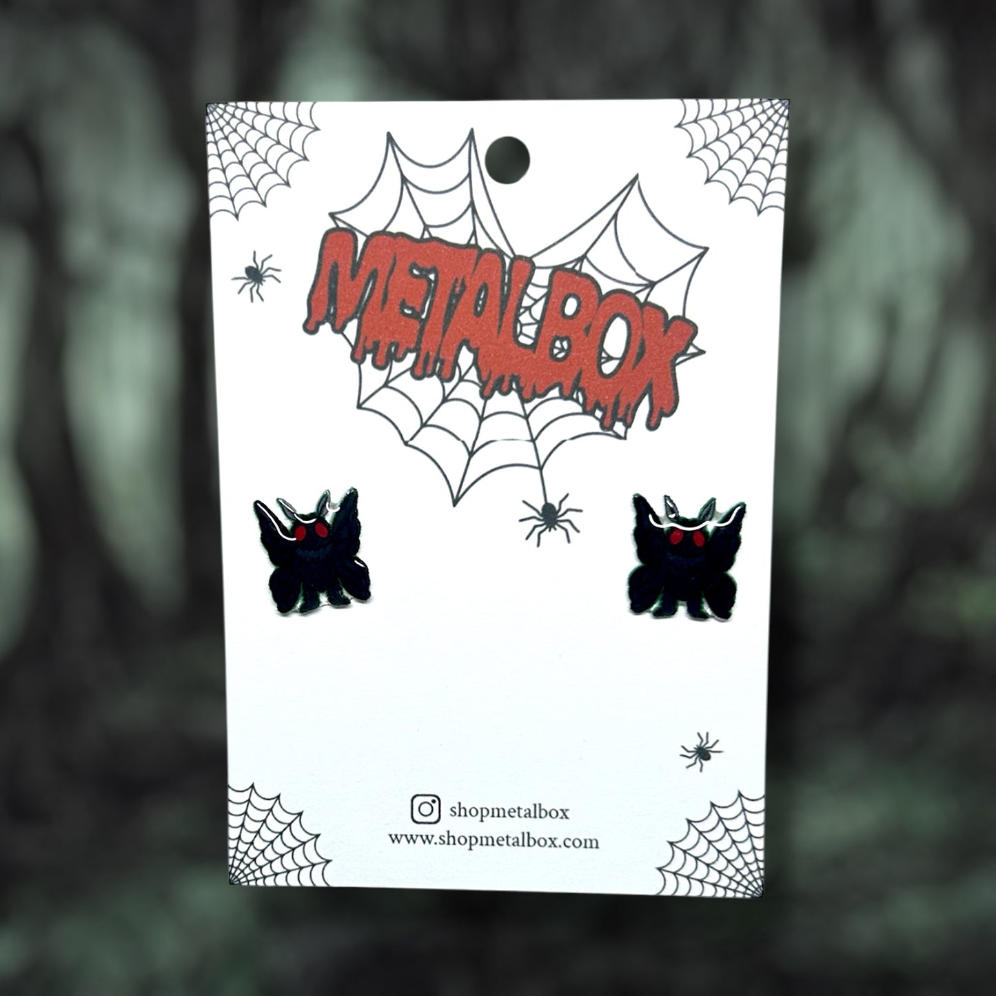 Mothman cryptid stud earrings on a blurred background.