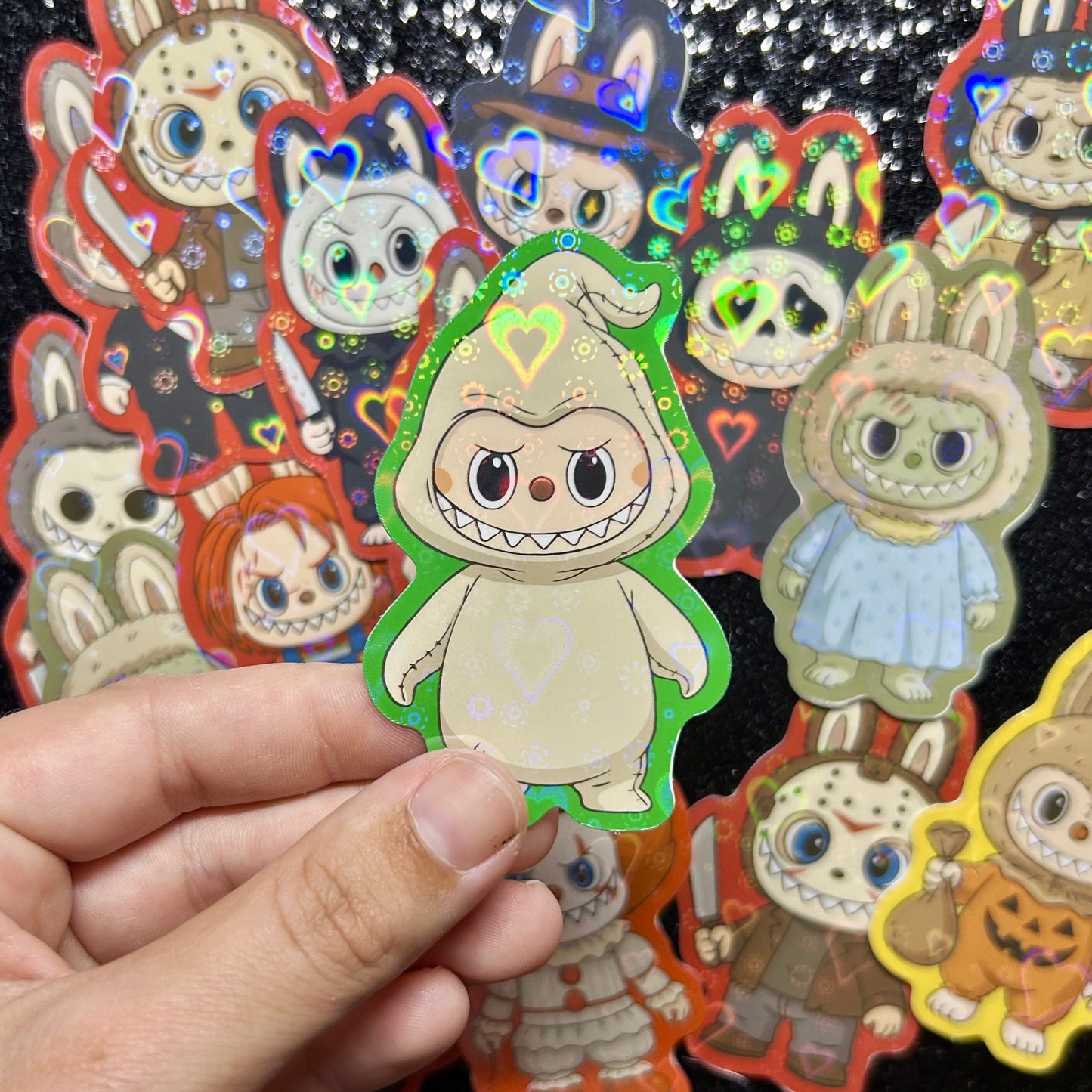 Hand holding a sticker of a Nightmare Before Christmas Oogie Boogie Labubu sticker, surrounded by other colorful stickers on a black background