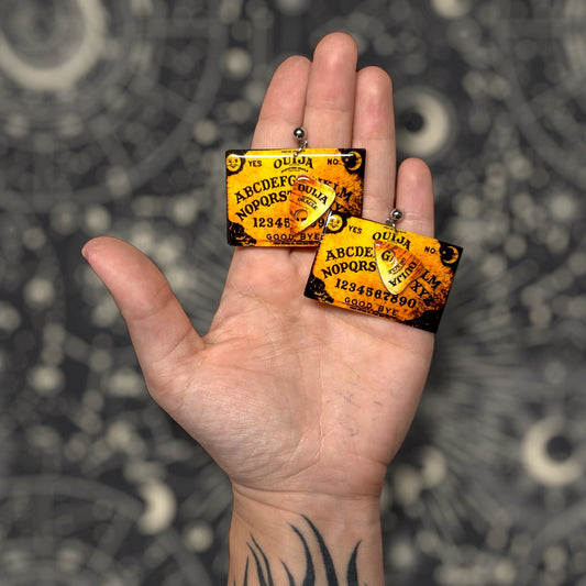Witchy Ouija board and planchette resin statement earrings being held