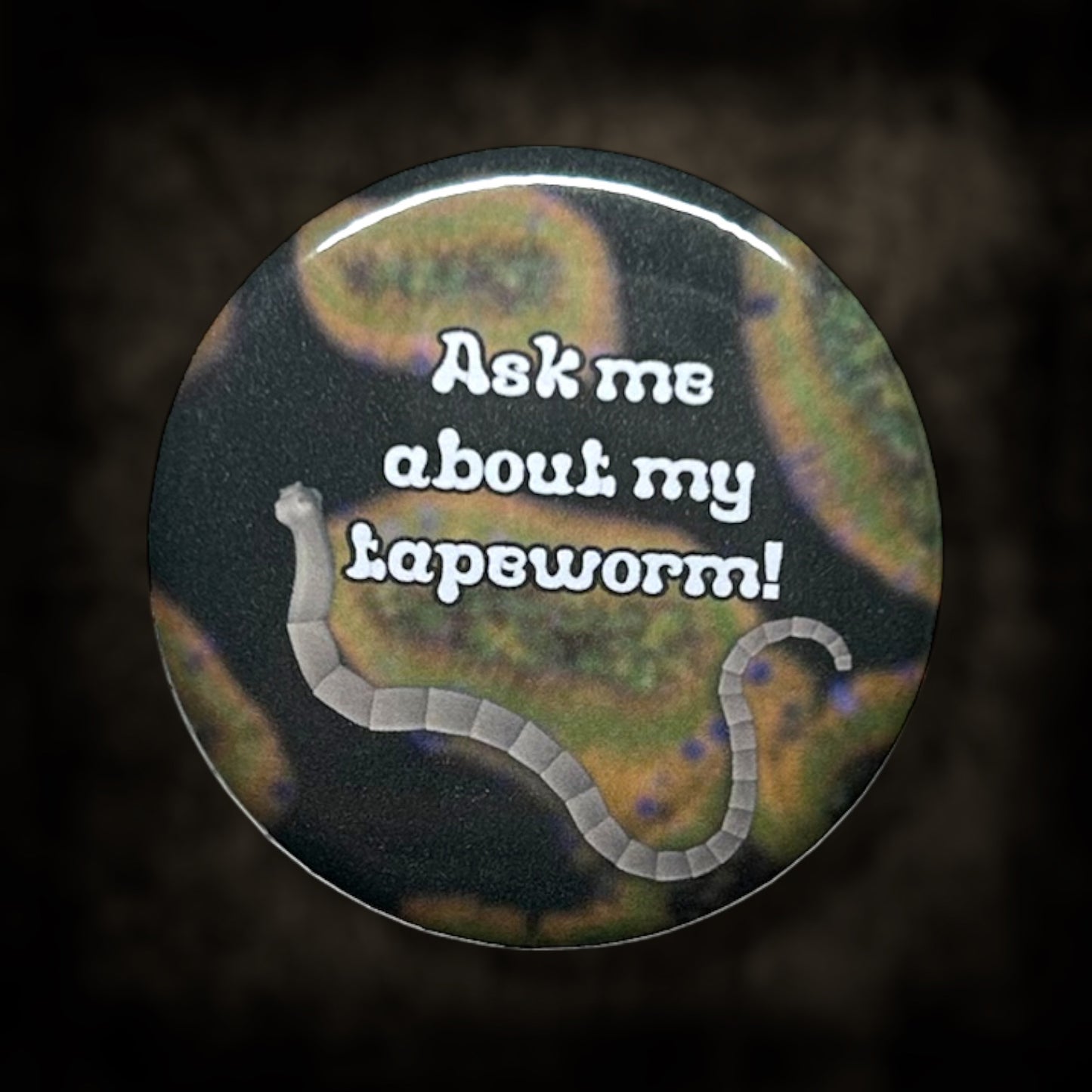 Button badge with text 'Ask me about my tapeworm!' on a dark background