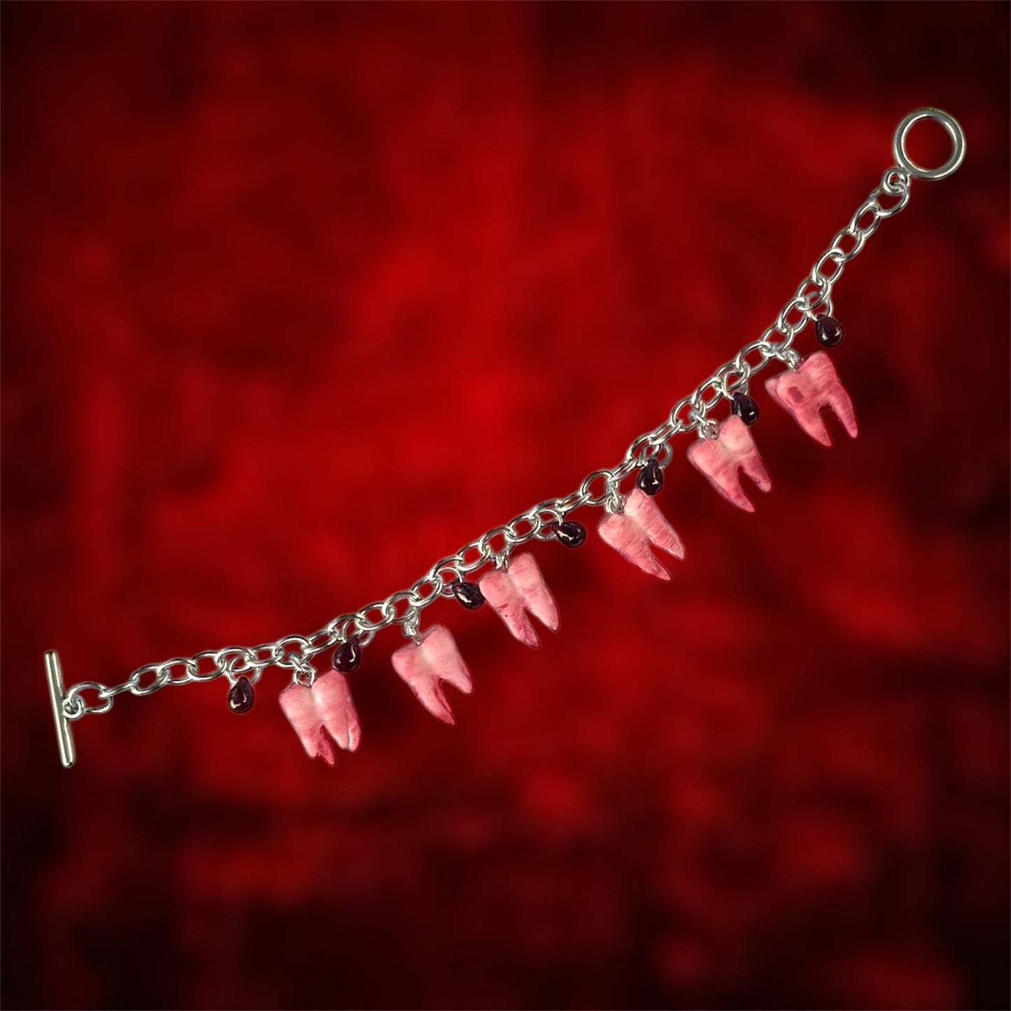 Unfastened bloody molars and blood drops charm bracelet on a blurred red background