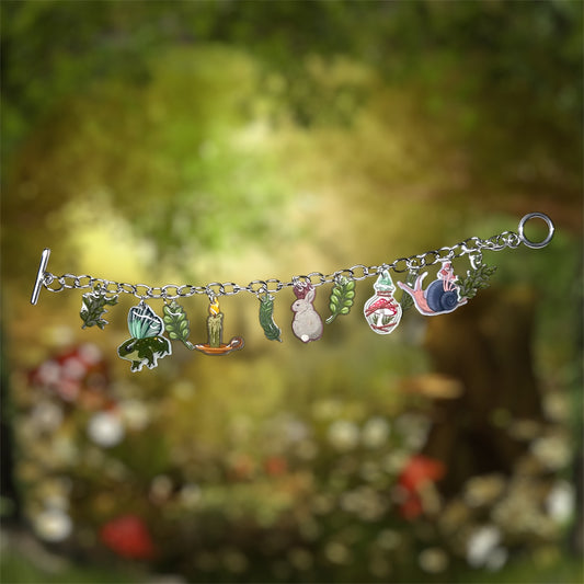 Witchy forest cottagecore charm bracelet with various charms including a frog, caterpillar, rabbit, snail, and leaves on a blurred natural background.