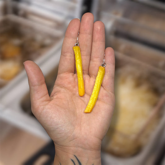 Hand holding a pair of realistic French fry dangle earrings on a blurry background