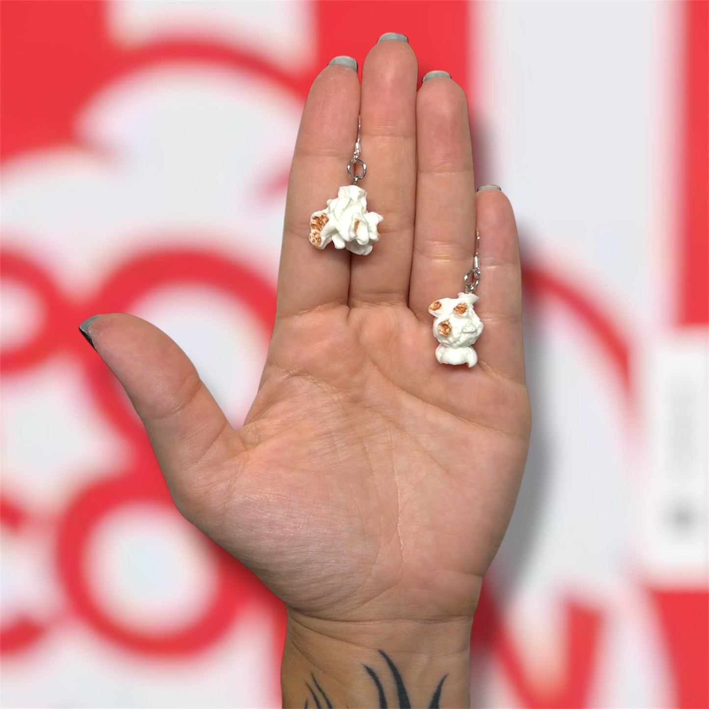 Hand holding a pair of plain popcorn dangle earrings on a red and white popcorn bucket background
