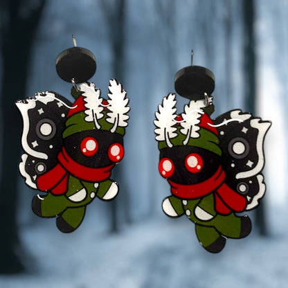 A pair of decorative earrings featuring a moth-like design with a red and black color scheme, wearing a snowsuit, with a forest background.