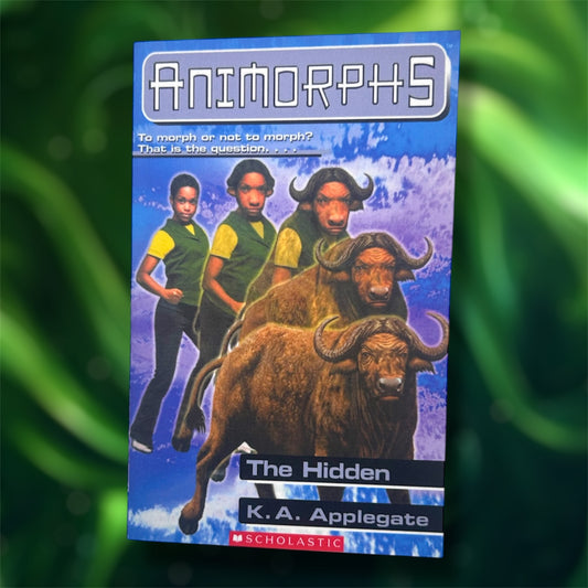 The front cover of a pocket notebook of Animorphs The Hidden on a blurred green background 