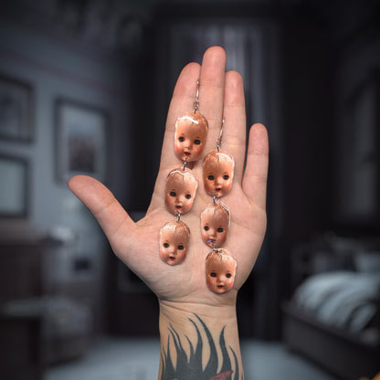 Creepy baby doll head stacked resin statement earrings being held