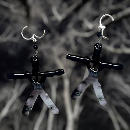 Blair Witch Project stick figure earrings depicting Heather's confessional on a blurred forest background.