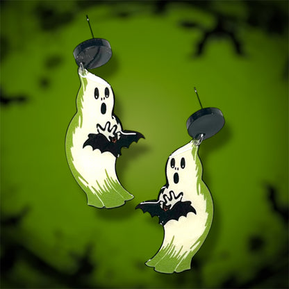 Glowing Halloween blow mold ghost holding a bat earrings on a blurred green background.