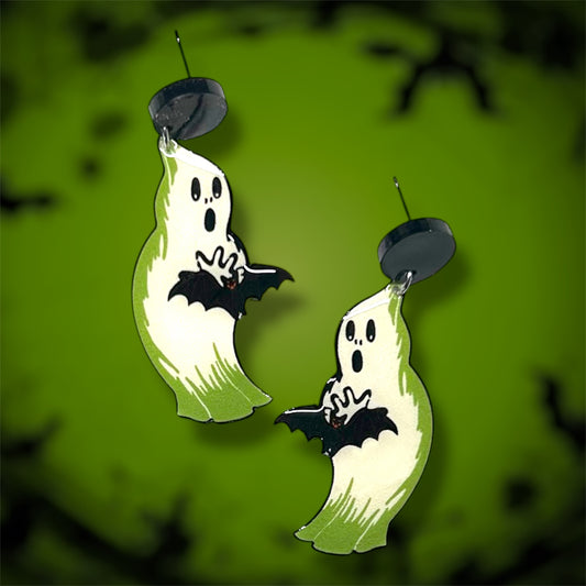 Glowing Halloween blow mold ghost holding a bat earrings on a blurred green background.