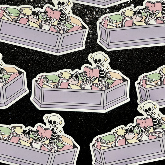 Stickers of a skeleton sitting in a coffin full of books reading a book on a black background