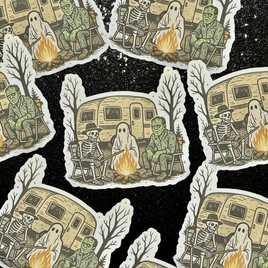 Stickers of a skeleton wearing a cowboy hat, a ghost, and Frankenstein sitting around a campfire with a camper in the background on a black background