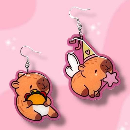 Taco capybara and princess capybara earrings on a pink background.