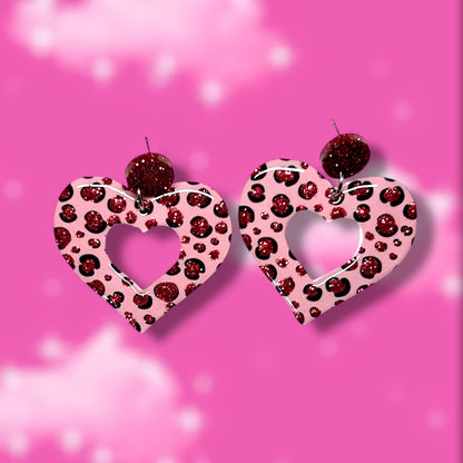 Glittery pink cheetah-print mod heart-shaped earrings on a blurred pink background.