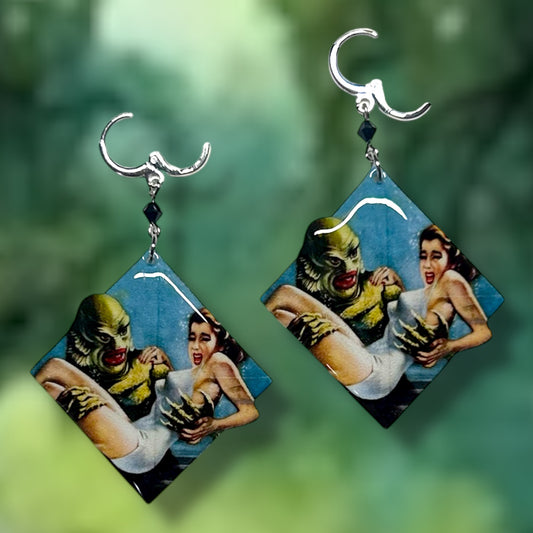 Creature from the Black Lagoon earrings on a blurred green background.