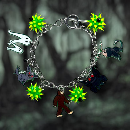 Bracelet with cryptids including the Fresno nightcrawler, Chupacabra, Bigfoot, Mothman, and the Jackalope and spiky green rubber beads on a dark background.