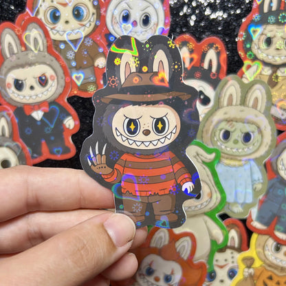 Hand holding a sticker of a Nightmare on Elm Street Freddy Krueger Labubu sticker, surrounded by other colorful stickers on a black background