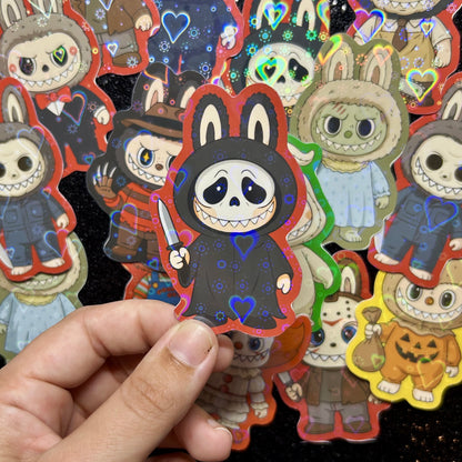 Hand holding a sticker of a Scream Ghostface Labubu sticker, surrounded by other colorful stickers on a black background