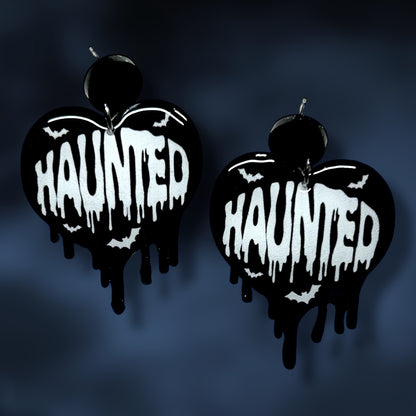 Heart-shaped Halloween earrings with 'HAUNTED' text and bats on a dark background