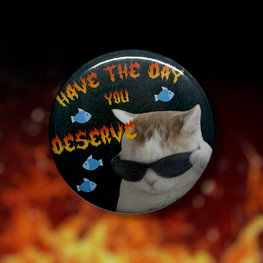 Pinback button of a cat wearing sunglasses and blue fish swimming around with orange and red flame text that reads "HAVE THE DAY YOU DESERVE" on  fiery background.