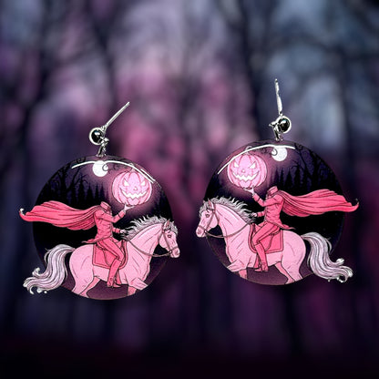 Pink Halloween headless horseman pink pumpkin jack o lantern earrings on a dark blurry background.