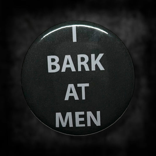 Black pinback button with white text that read "I BARK AT MEN" on a blurred black and white background.