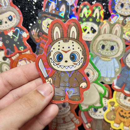 Hand holding a sticker of a Friday the 13th Jason Voorhees Labubu sticker, surrounded by other colorful stickers on a black background