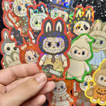 Hand holding a sticker of a Texas Chainsaw Massacre Leatherface Labubu sticker, surrounded by other colorful stickers on a black background