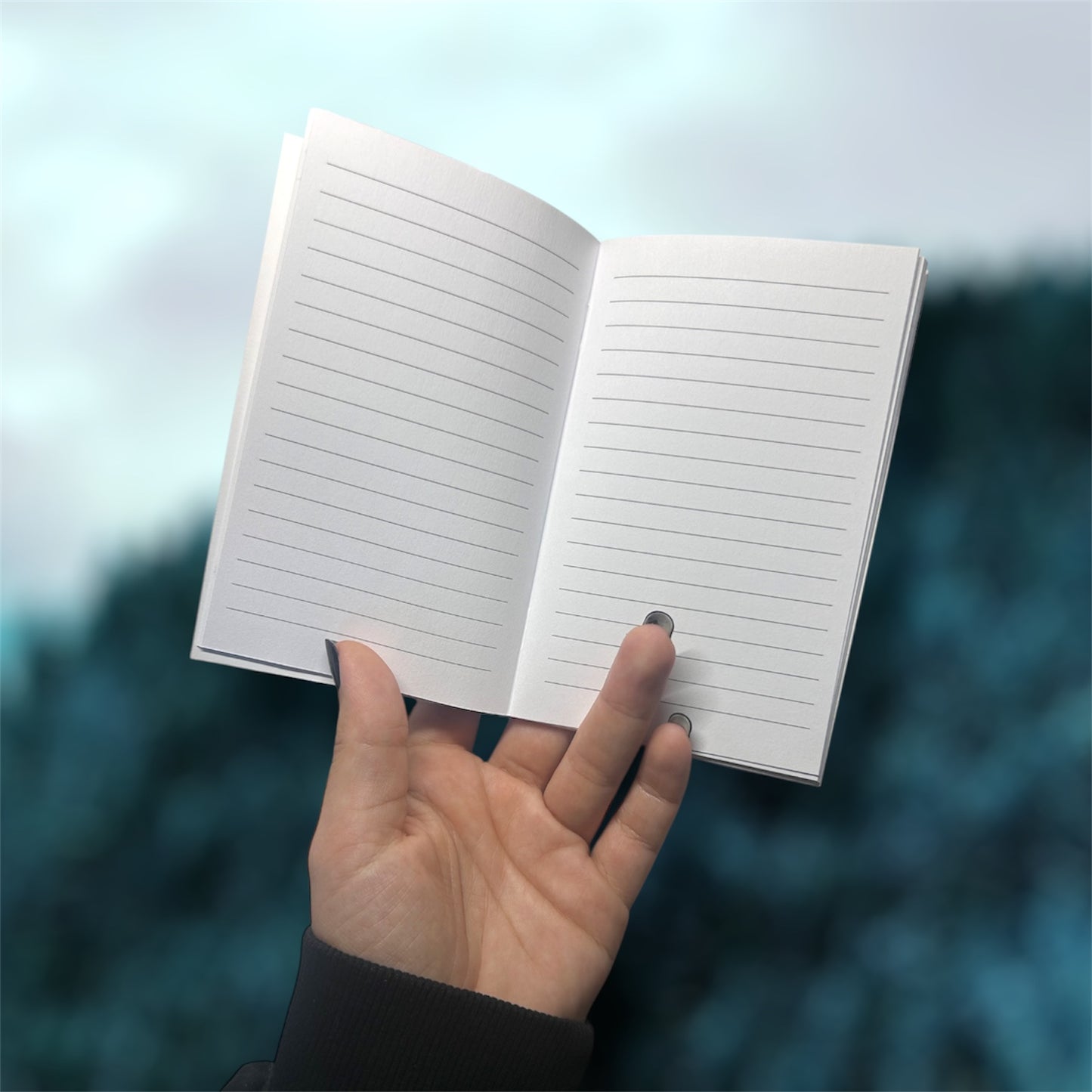Hand holding an open pocket notebook with lined pages on a blurred blue background
