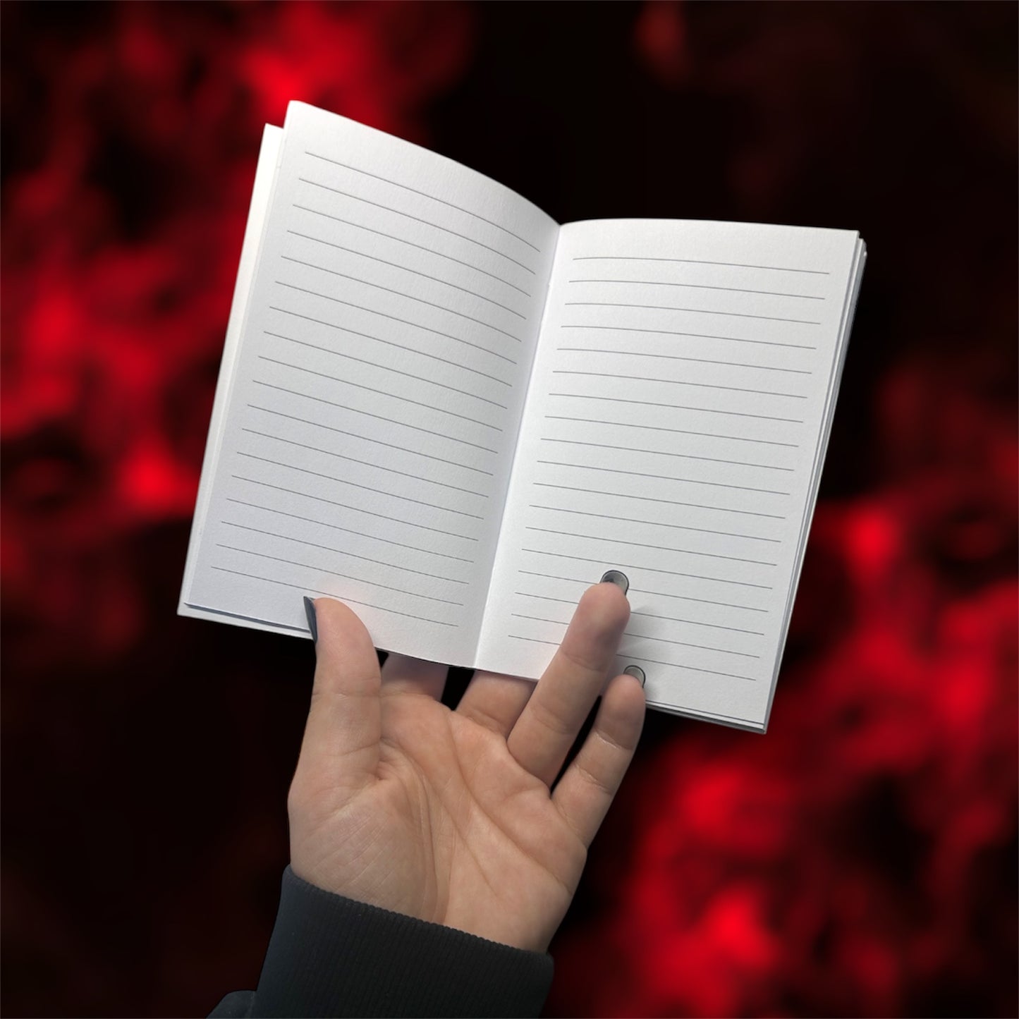 Hand holding an open pocket notebook with lined pages on a blurred red and black background