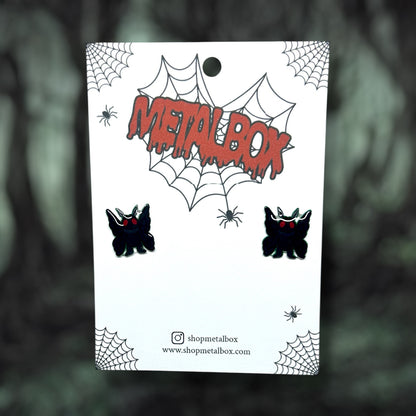 Mothman cryptid stud earrings on a blurred background.