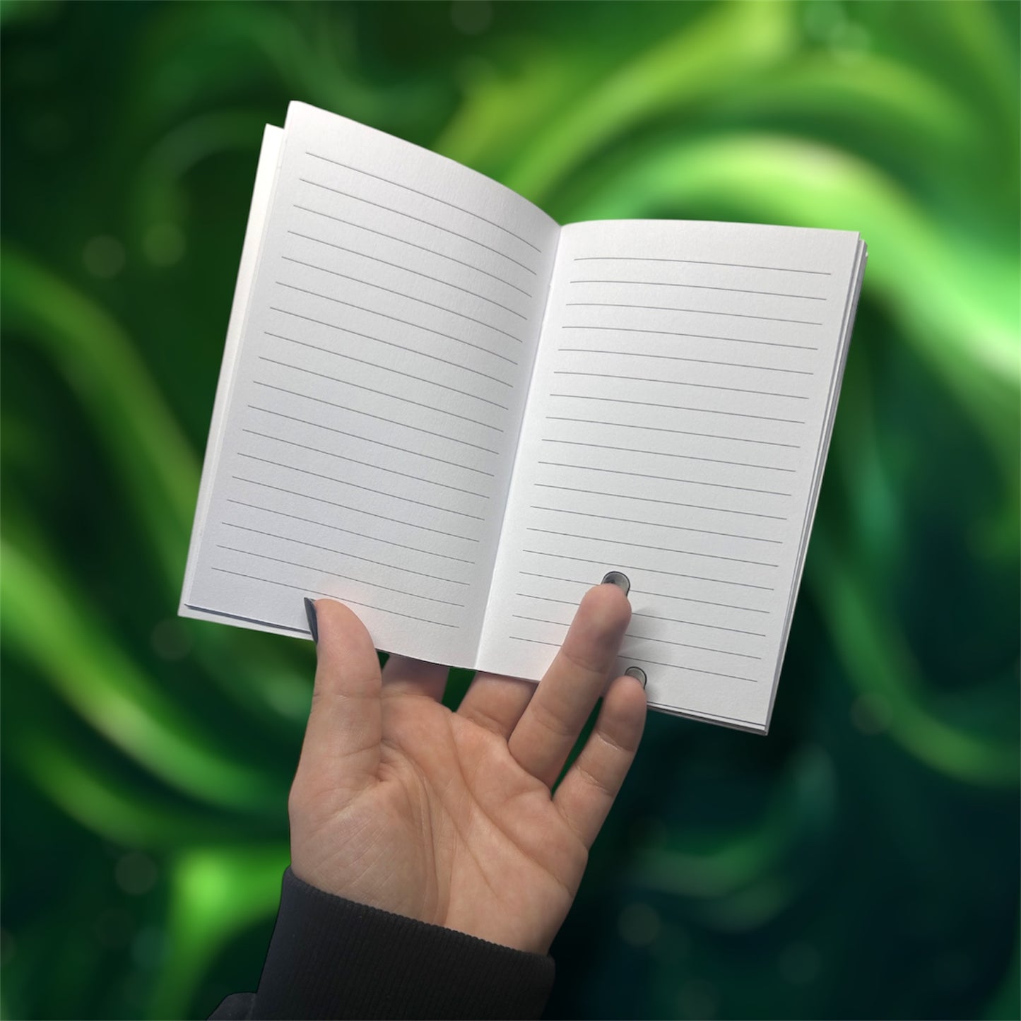 Hand holding an open pocket notebook with lined pages on a blurred green background