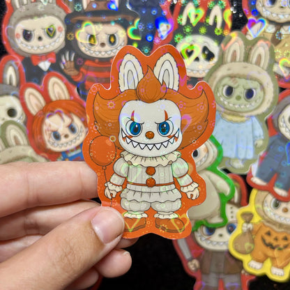 Hand holding a sticker of an IT Pennywise Labubu sticker, surrounded by other colorful stickers on a black background