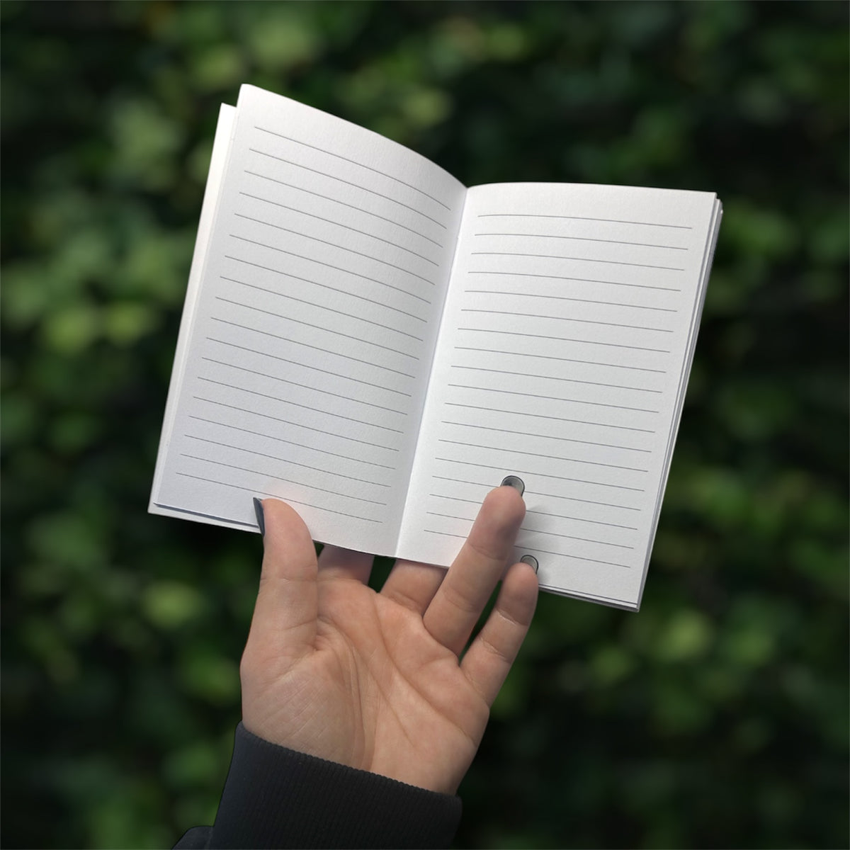 Hand holding an open notebook with lined pages against a blurred green background