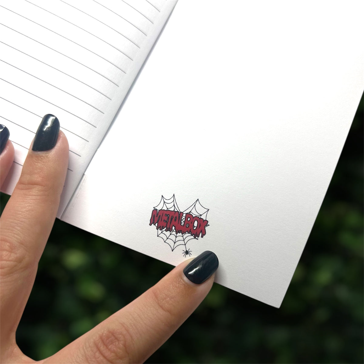 Hand holding open a notebook with Metalbox logo on back cover on a blurred green background