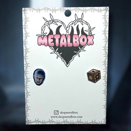 Hellraiser Pinhead face and lament configuration box stud earrings on blurred blue background.