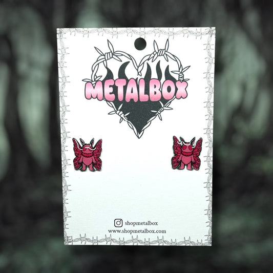 Pink Mothman cryptid stud earrings on a blurred background.