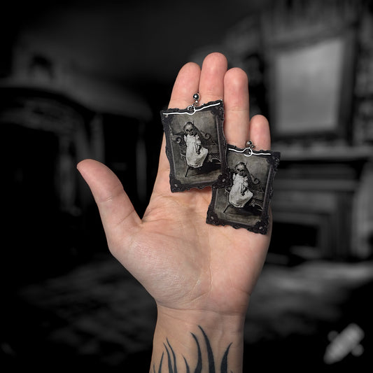 A pair of earrings featuring a vintage black and white framed art of a spooky pumpkin-headed baby being held. 