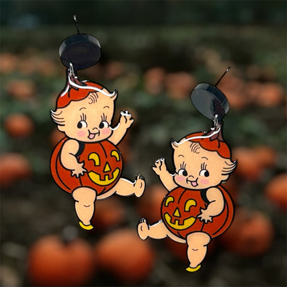 Halloween cherub baby kewpie pumpkin jack-o-lantern earrings on a blurred pumpkin patch background.