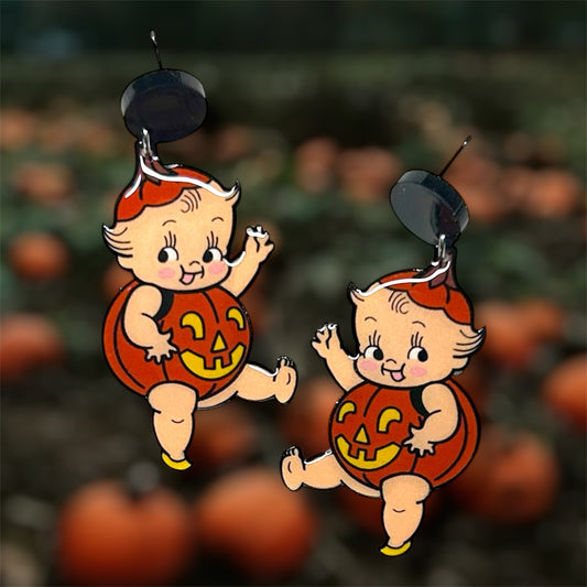 Halloween cherub baby kewpie pumpkin jack-o-lantern earrings on a blurred pumpkin patch background.