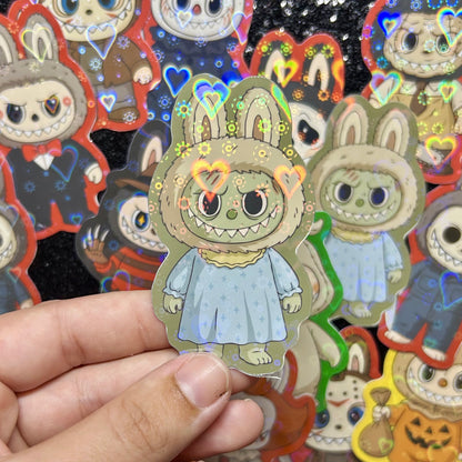 Hand holding a sticker of a The Exorcist Regan MacNeil Labubu sticker, surrounded by other colorful stickers on a black background