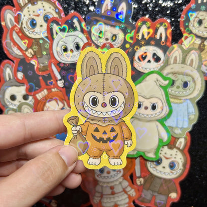 Hand holding a sticker of a Trick-r-Treat Sam Labubu sticker, surrounded by other colorful stickers on a black background