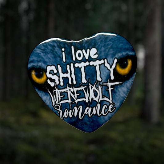 Heart-shaped button with text 'I LOVE SHITTY WEREWOLF ROMANCE' against a blurred forest background