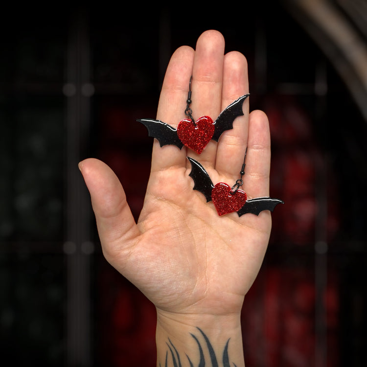 Glittery red and black bat wing heart goth Valentine's Day Valloween resin statement earrings being held