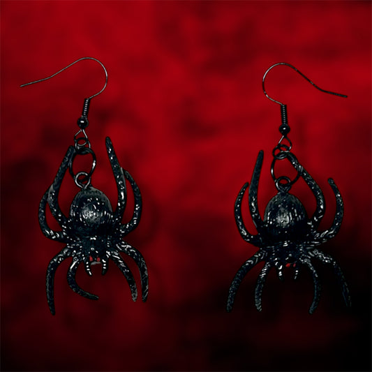 Black spiders with red eyes earrings on a blurred red and black background.
