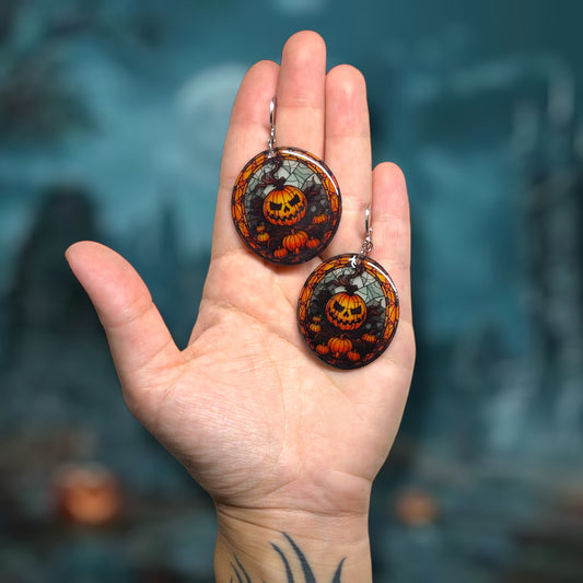 Hand holding Halloween stained glass pumpkin jack o lantern earrings on a dark background